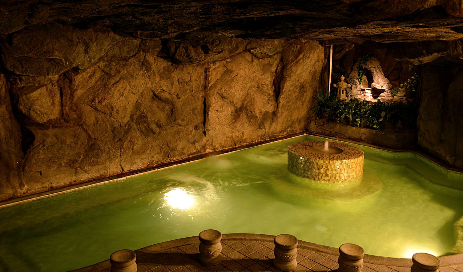 The natural hot spring pool at Beverly Wellness Hot Springs, glowing green inside its stone grotto